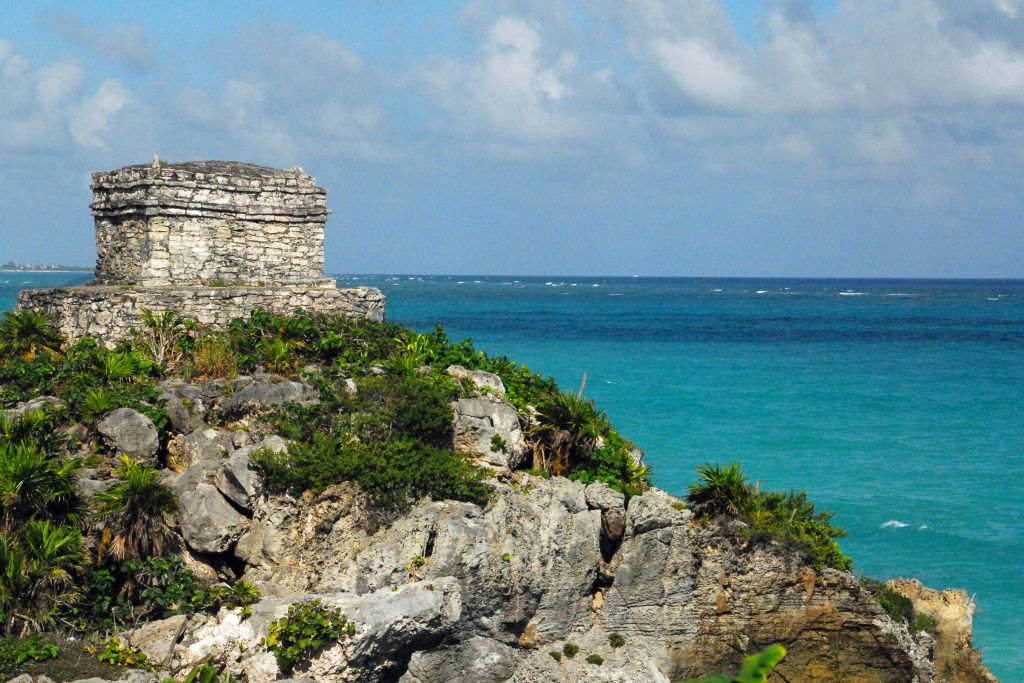 A Rocky Island In The Middle Of A Body Of Water With Tulum In The Background